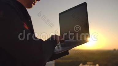一个有笔记本电脑的程序员坐在屋顶上，在日落时写代码。 远程工作自由职业者。 工作自由。 打字